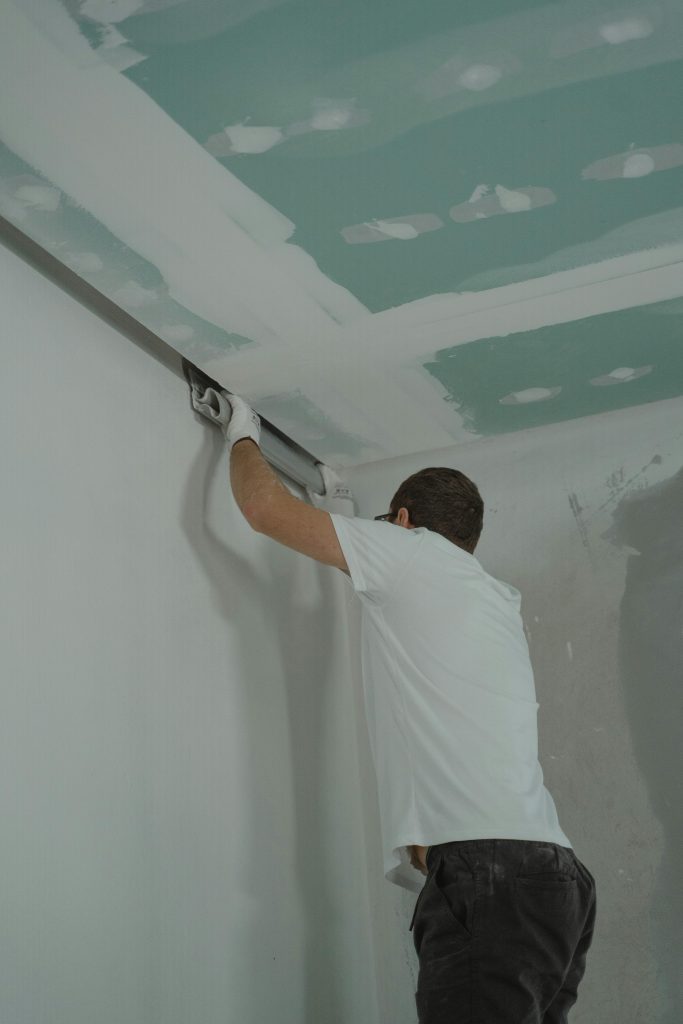 A man works meticulously on drywall installation during a house renovation. Un homme travaille avec soin sur l'installation de cloisons sèches lors d'une rénovation domiciliaire.
