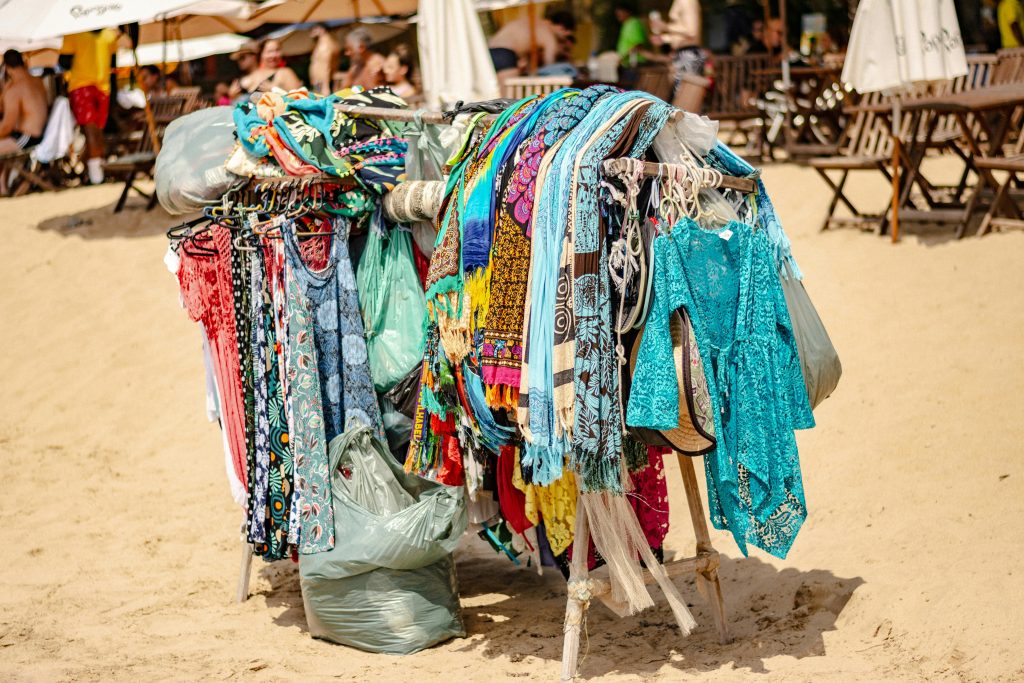 Vibrant clothing stand on beach showcasing colorful garments with sandy background. Étalage de vêtements vibrants sur la plage présentant des vêtements colorés avec un arrière-plan sablonneux.