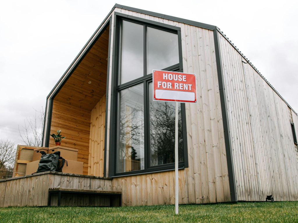 Low-angle view of a modern wooden house with a 'House for Rent' sign, showcasing contemporary architecture. Vue de bas en haut d'une maison en bois moderne avec une pancarte « Maison à louer », mettant en avant l'architecture contemporaine.