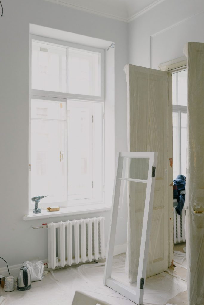 Window frame on floor near wooden doors and heating system in light apartment during renovation process Cadre de fenêtre sur le sol près des portes en bois et du système de chauffage dans un appartement clair lors du processus de rénovation