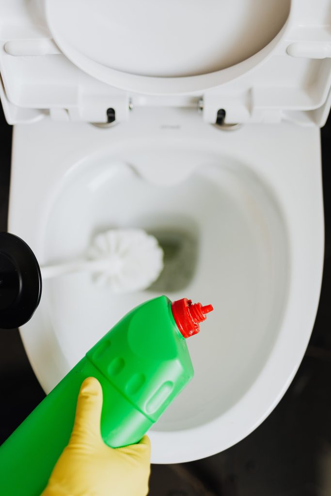Top view crop anonymous person wearing yellow cleaning gloves cleaning toilet while pouring liquid detergent from green bottle in toilet bowl Vue de dessus d'une personne anonyme portant des gants de nettoyage jaunes nettoyant les toilettes tout en versant du détergent liquide d'une bouteille verte dans la cuvette des toilettes