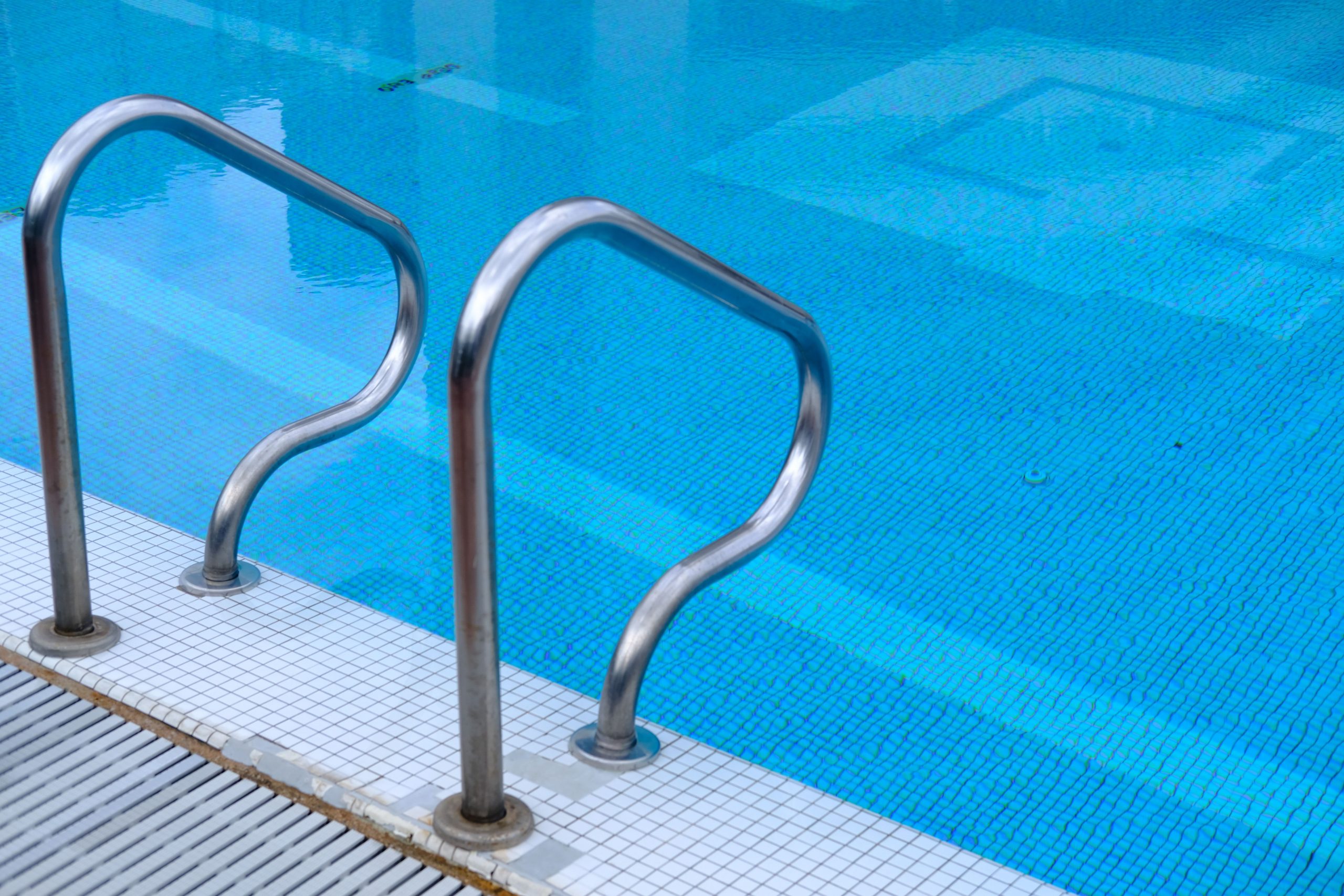 Échelle inox dans piscine eau claire et carrelage bleu