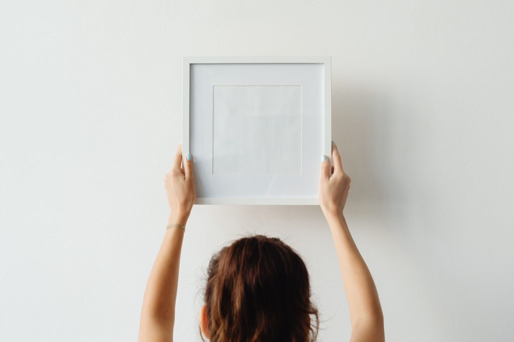 Femme accrochant cadre vide mur blanc